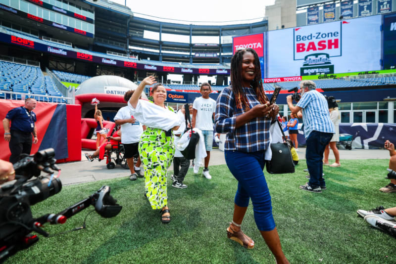 A diverse group of people at a stadium event with a large digital screen displaying "Bed-Zone BASH" and sponsor logos like Toyota and Gillette in the background.