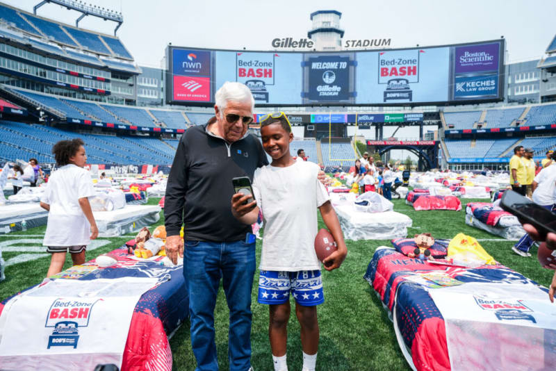 Two people standing on a football field inside Gillette Stadium during Bed-Zone Bash event, surrounded by beds with blankets and toys.