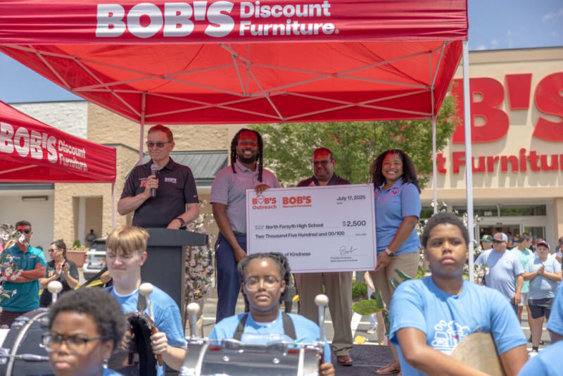 Bob's Discount Furniture outdoor event with a large check presentation for $2,500 to North Forsyth High School, featuring staff under branded red tents.