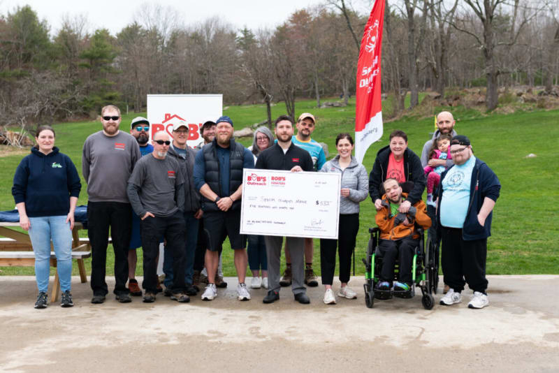 Group of people standing outdoors holding a large check from Bob's Outreach for $582 made out to Special Olympics Maine, with a red Bob's banner in the background.