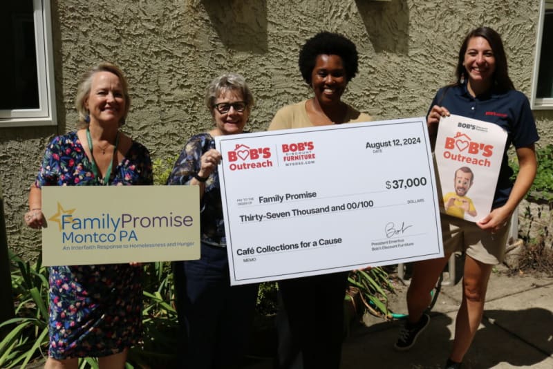 Four people holding signs and a large check from Bob’s Discount Furniture, dated August 12, 2024, showing a $37,000 donation to Family Promise Montco PA for Café Collections for a Cause. The signs include “Family Promise Montco PA An Interfaith Response to Homelessness and Hunger” and “BOB’S Outreach.”