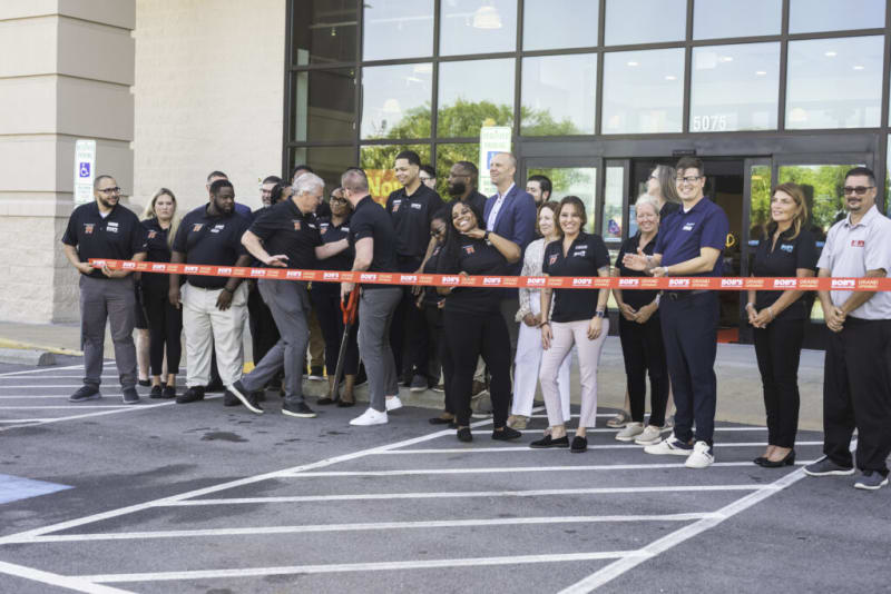 Group of people standing outside a commercial building during a ribbon-cutting ceremony for the grand opening of Bob's store.