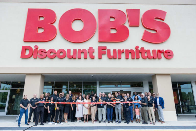 BOB'S Discount Furniture storefront with a large red sign and a group of people gathered for a ribbon-cutting ceremony.