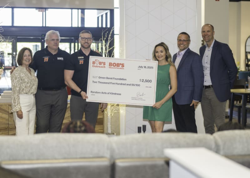 Six people stand indoors holding a large check from BOB'S Discount Furniture dated July 18, 2025, made out to Green Beret Foundation for $2,500 for Random Acts of Kindness.