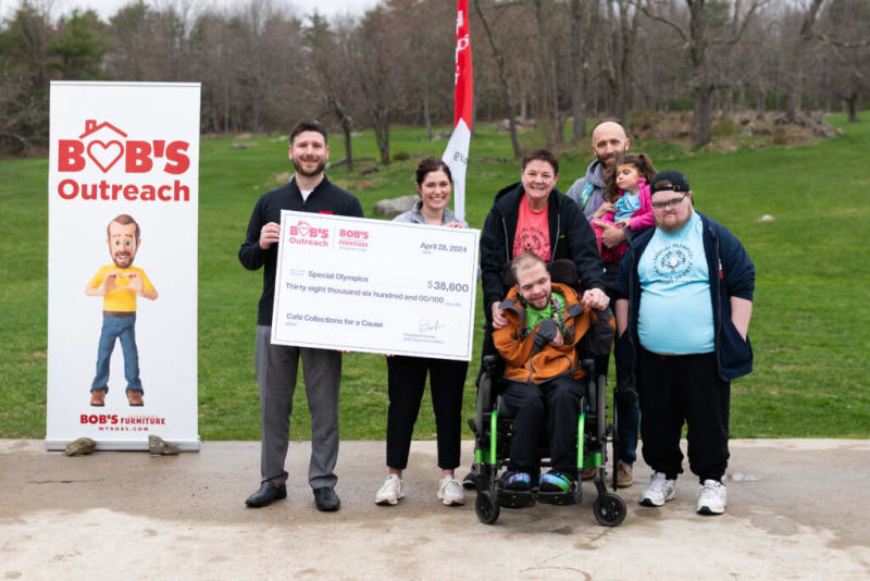 Group of people holding a large check for $38,600 made out to Special Olympics from Bob's Furniture, next to a Bob's Outreach banner.