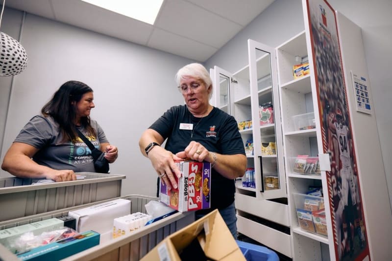 Two women organizing food items in a pantry with white shelves; one holds a box of Bob's Red Mill P.B. Bites, a gluten-free snack with 10 grams of protein.