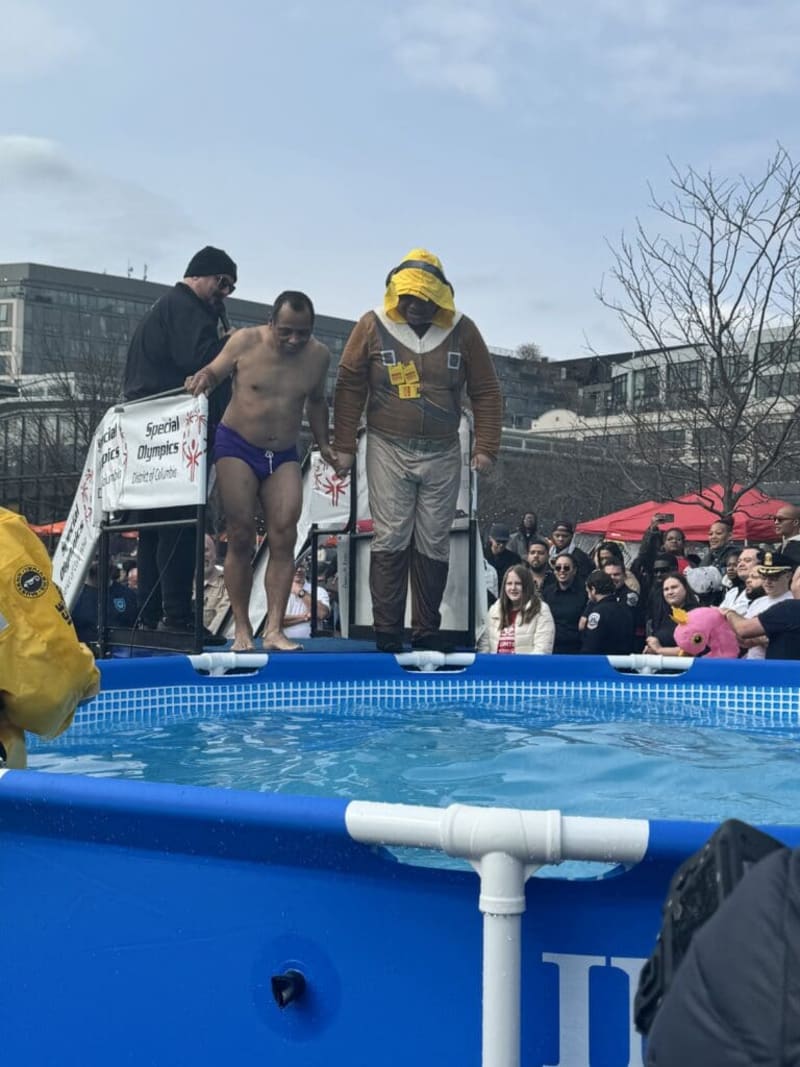 Two men stand on a platform above a blue pool preparing for a plunge during a Special Olympics event in Washington, D.C., with a crowd watching.