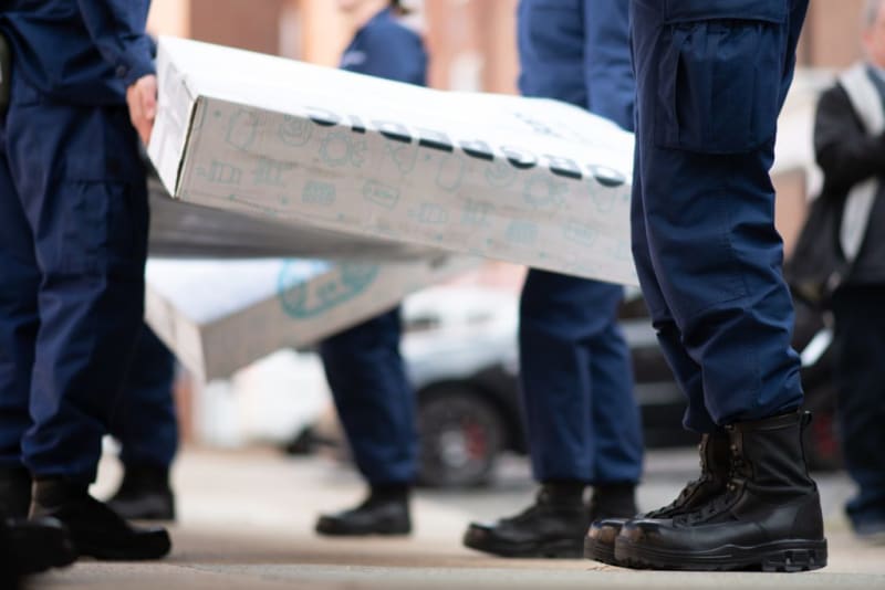 People in navy blue uniforms and black boots carrying large white boxes outdoors, emphasizing teamwork and coordinated effort in logistics or delivery.