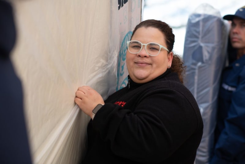 Person wearing a black fleece jacket and smartwatch, pressing or smoothing a large sheet of translucent plastic against a wall.