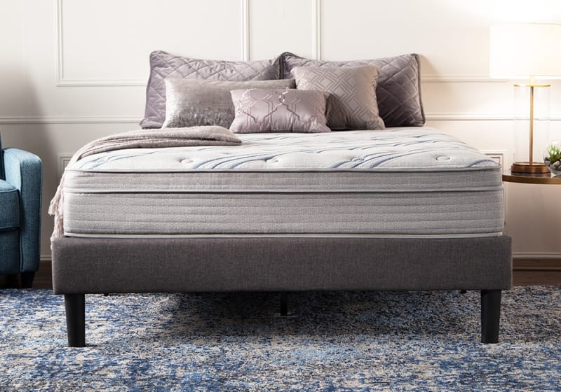 Queen-size mattress with light gray fabric, quilted top with blue accents, on a dark gray upholstered platform bed frame, styled with decorative pillows and a throw blanket.