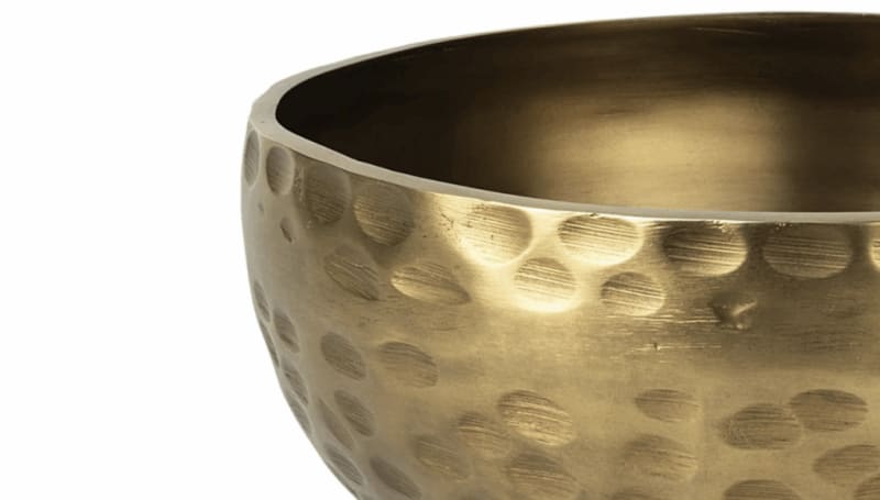 Brass singing bowl with hammered texture, golden finish, and smooth interior, used for meditation and sound therapy.