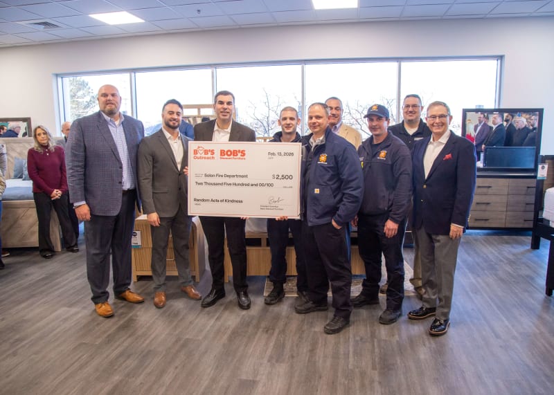 Group of people holding a large check from Bob's Discount Furniture Outreach for $2,500 to Solon Fire Department dated Feb. 13, 2026, in a furniture store setting.