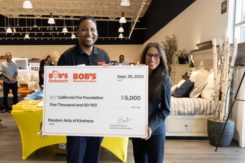 Two people holding a large check from Bob’s Discount Furniture dated Sept. 26, 2025, for $5,000 payable to California Fire Foundation for Random Acts of Kindness.