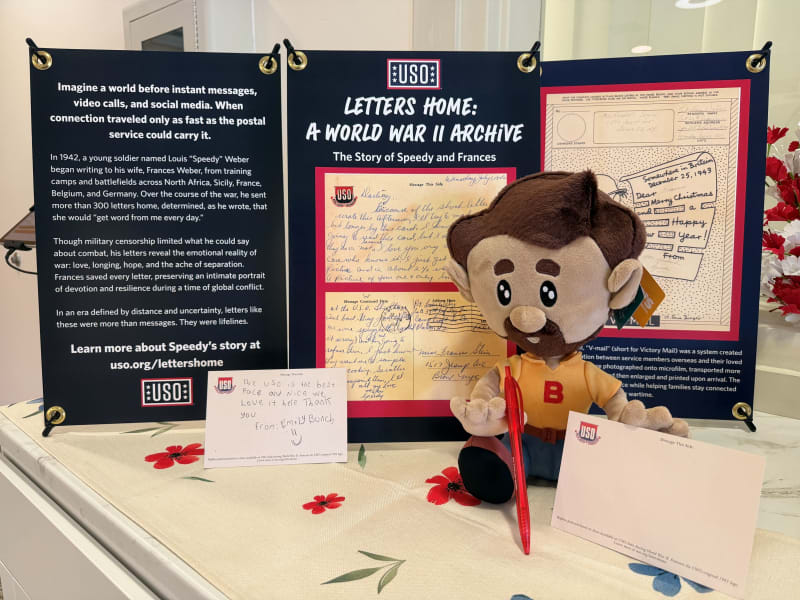 USO exhibit panel titled "Letters Home: A World War II Archive" detailing soldier Louis "Speedy" Weber's letters to his wife Frances, with a plush doll holding a red pen and two postcards, one handwritten note saying: "The USO is the best place and nice we love it here thank you from: Emily Bunch :)"
