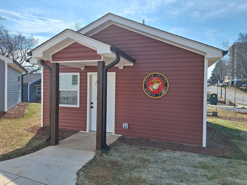 Small red single-story building with white trim and a white door, featuring a United States Marine Corps emblem on the front wall.