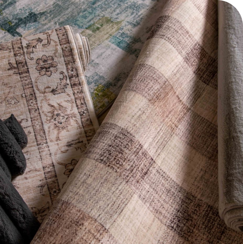 Rolled beige and brown patterned rugs with floral and plaid designs, showcasing textured woven fabric for home decor and flooring.