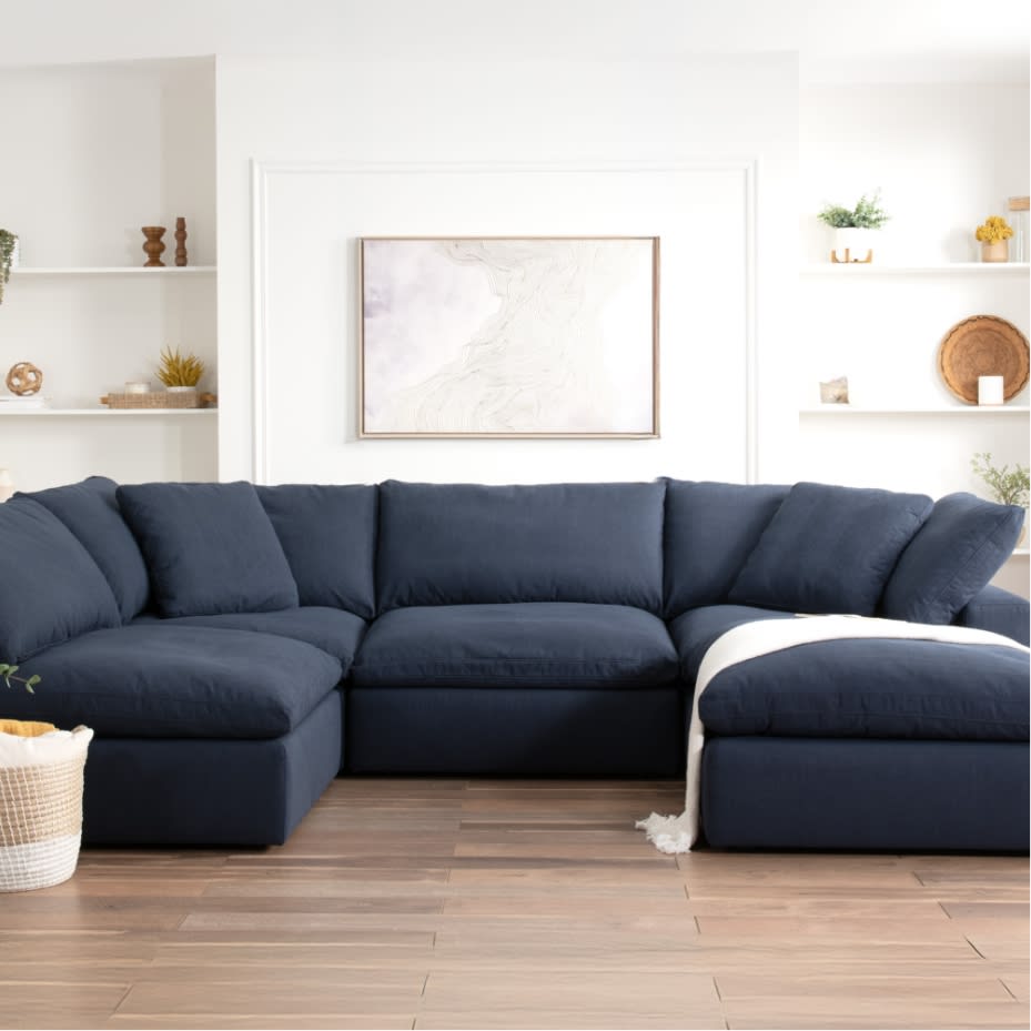 Modern navy blue sectional sofa with plush cushions and chaise lounge in a bright, minimalist living room featuring white walls and decorative shelves.