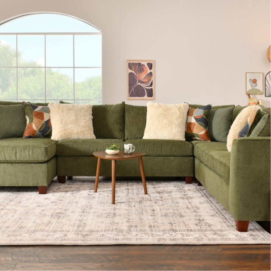 Modern living room with olive green fabric sectional sofa, multicolored geometric and cream throw pillows, wooden coffee table, and neutral textured rug.
