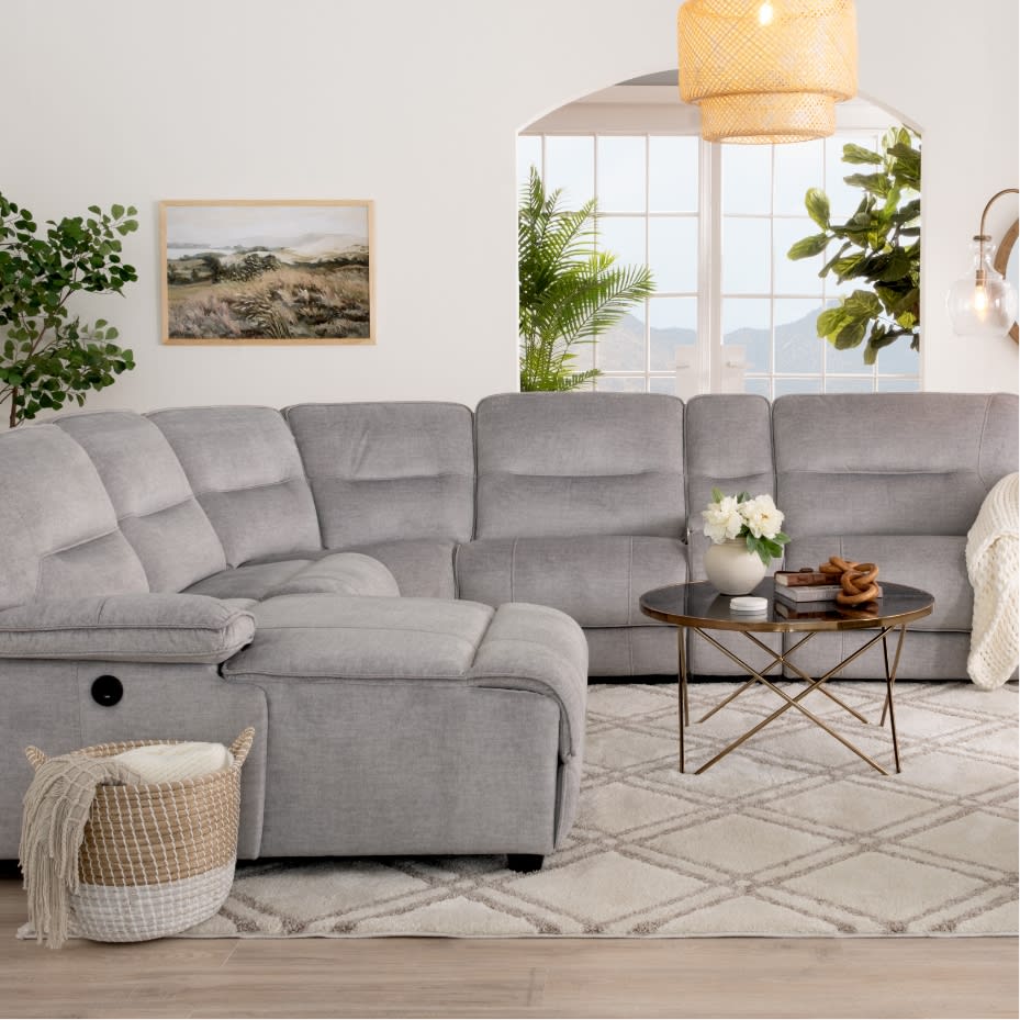Gray fabric sectional sofa with plush cushions and chaise lounge, paired with a round black metal coffee table on a patterned beige rug in a modern living room.