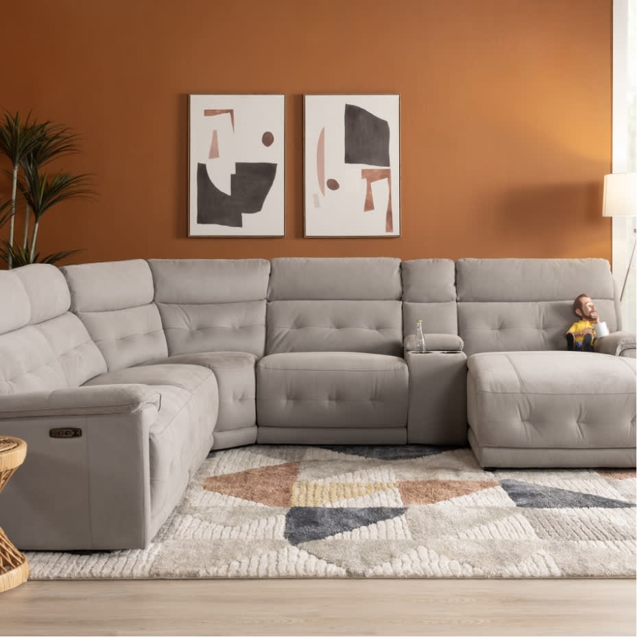 Modern L-shaped light gray fabric sectional sofa with tufted cushions, built-in cup holders, and a geometric patterned area rug in a warm living room.