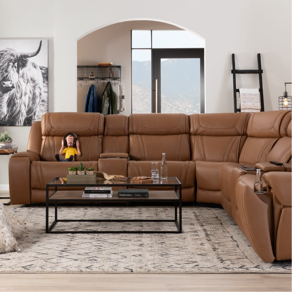 Brown leather sectional sofa with plush cushions and recliner features, paired with a black metal and glass coffee table on a patterned rug in a modern living room.