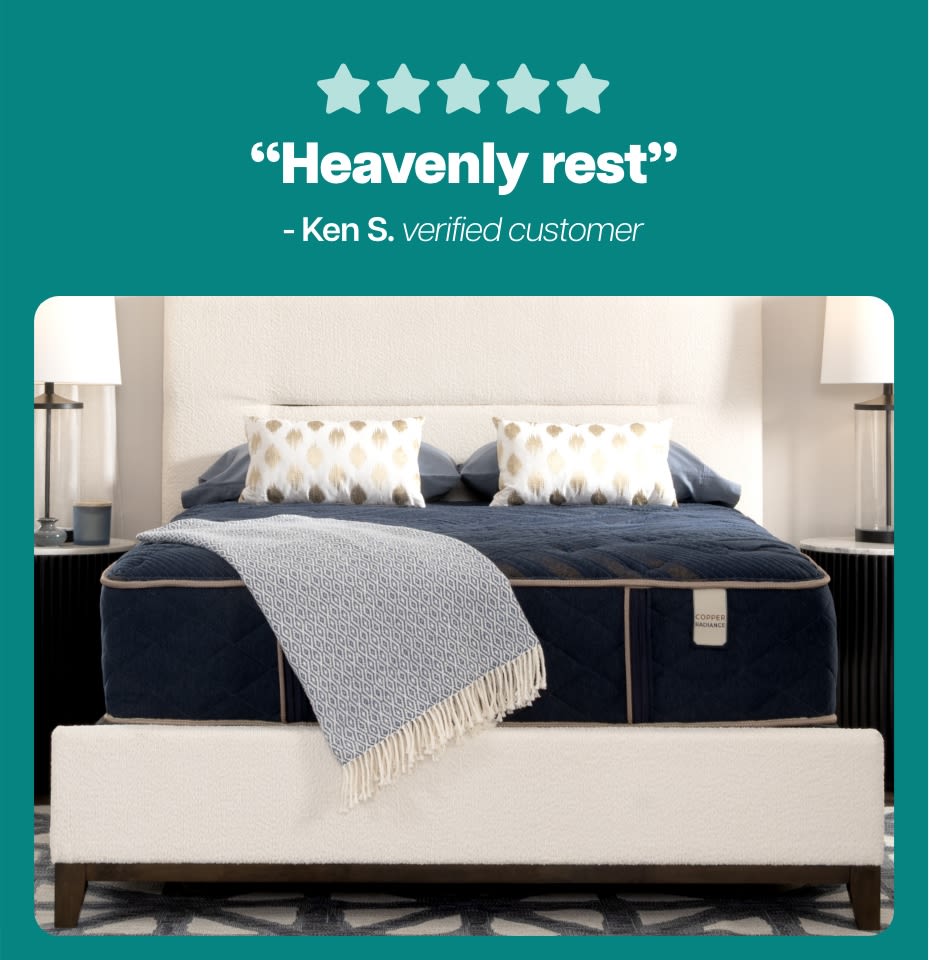 Five-star rating with the text “Heavenly rest” - Ken S. verified customer above a navy blue Copper Radiance mattress with beige trim on a cream upholstered bed frame, flanked by two lamps.