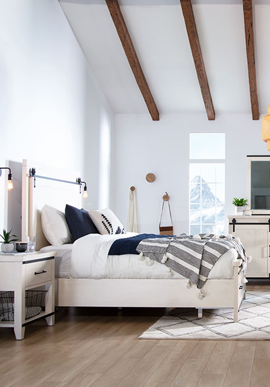 Beige bedroom set with white and blue bedding. Striped white and gray throw blanket on the end of the bed.