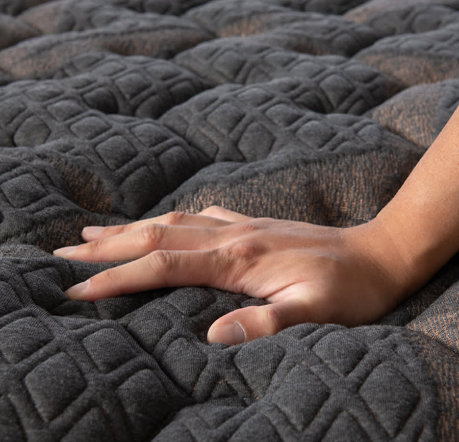 Hand pushing down on the top of a gray mattress to show this feel