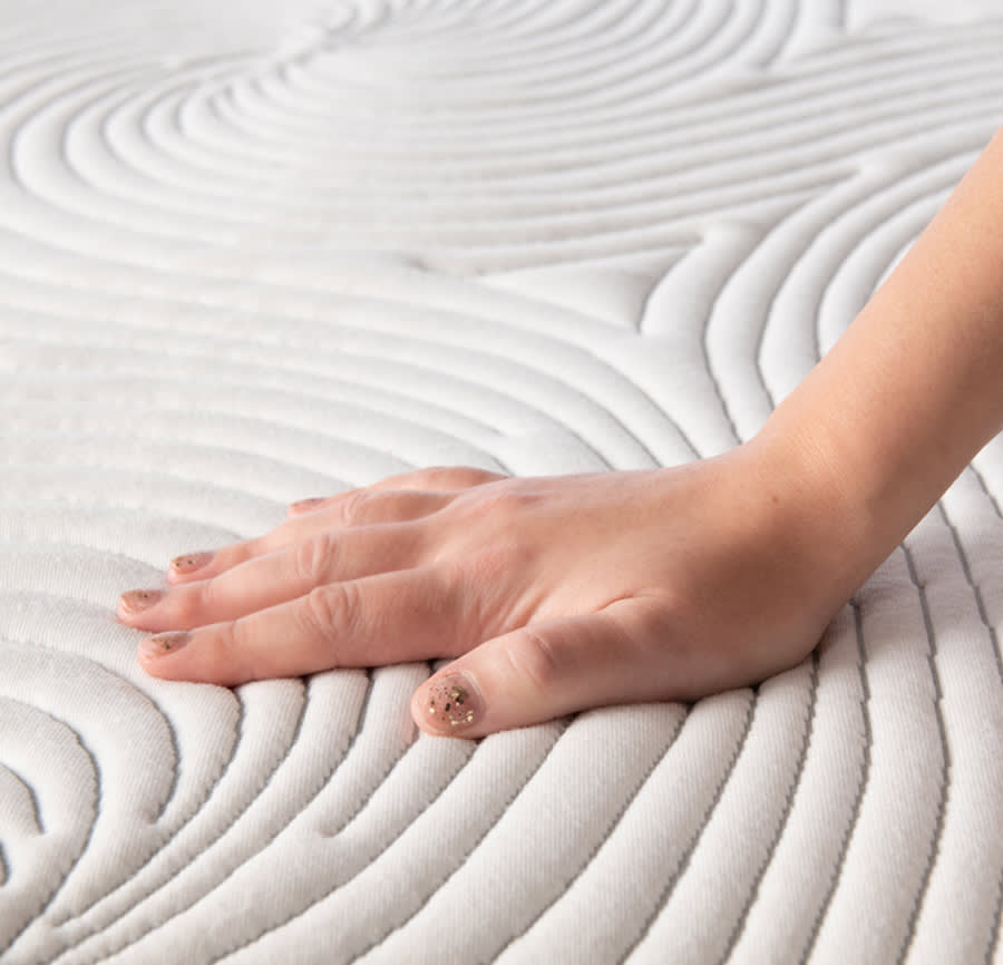 Hand pushing down on the top of a white mattress to show this feel