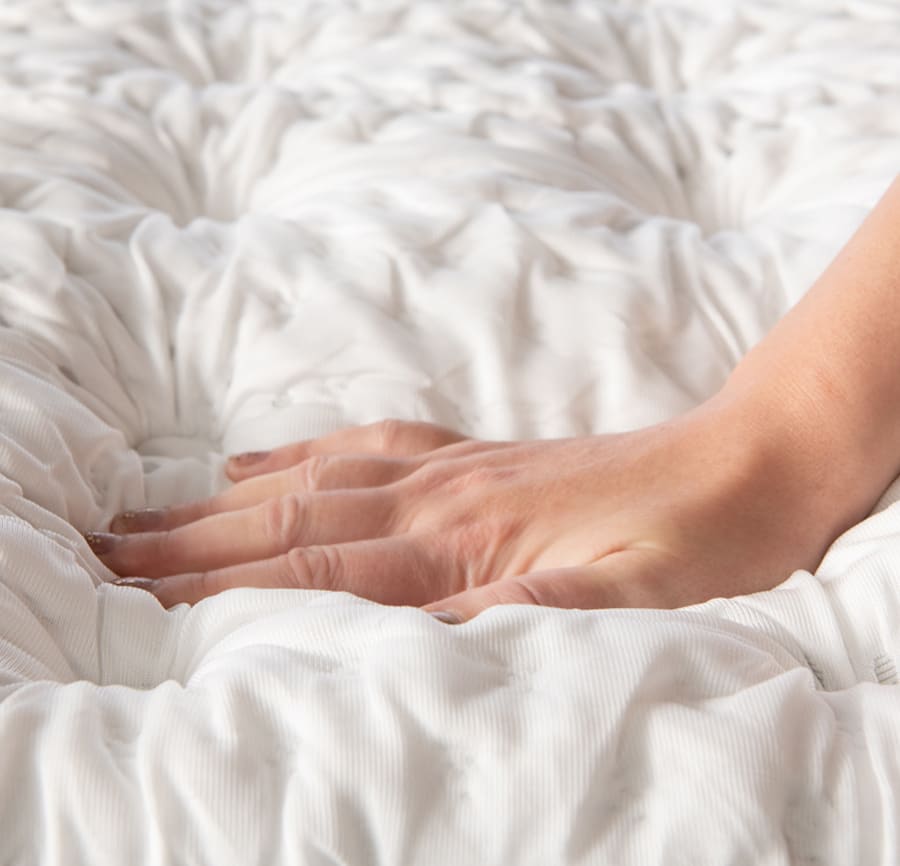 Hand pushing down on the top of a white mattress to show this feel