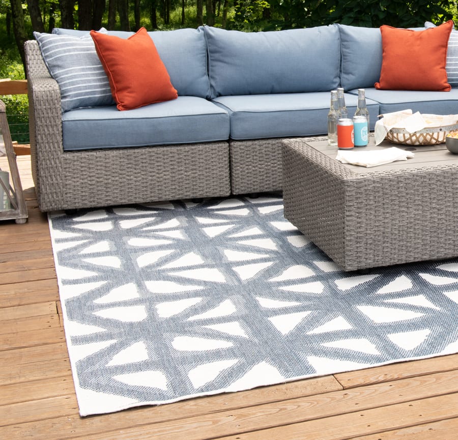 Outdoor sofa with accent pillows and ottoman on a large blue and white geometric indoor/outdoor rug.