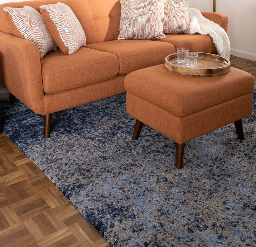 Orange sofa and ottoman with accent pillows on a blue abstract rug