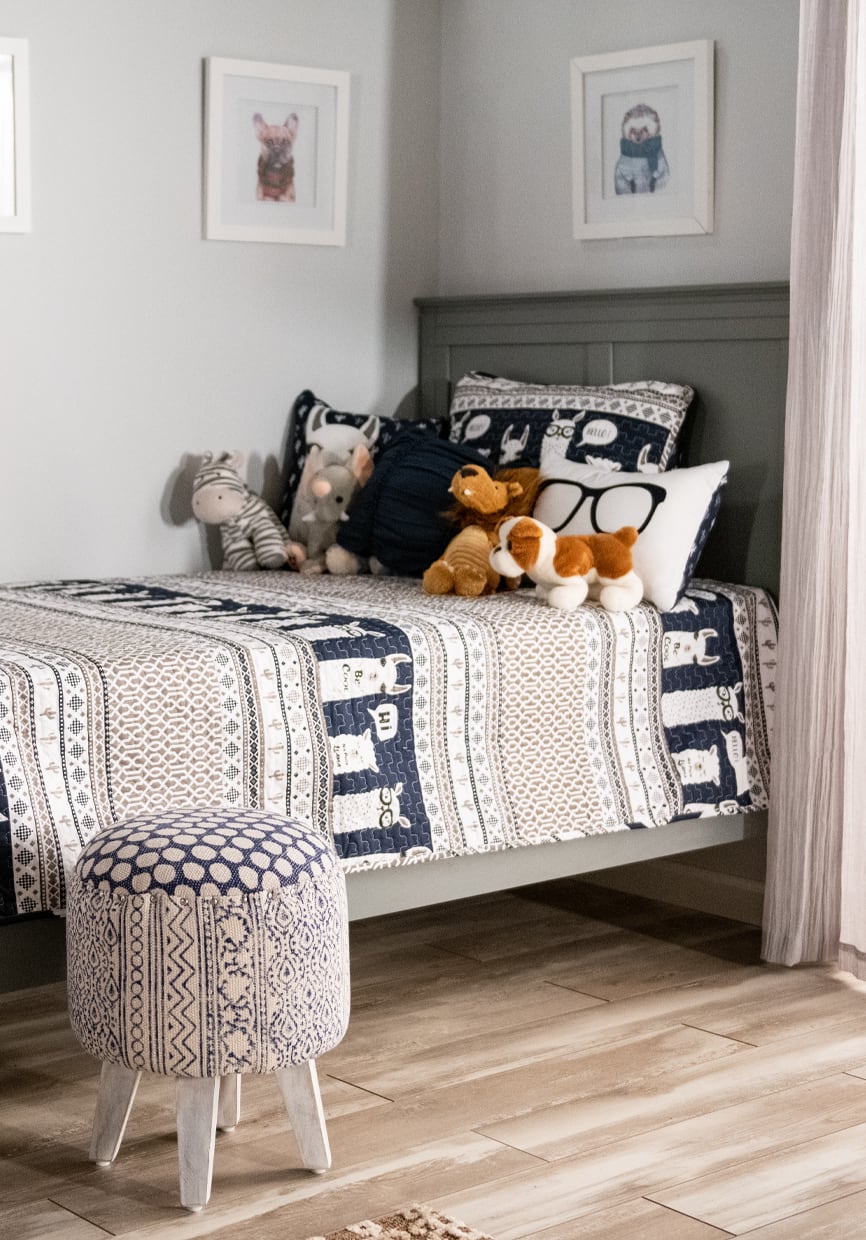 Gray twin size kids bed with llama print bedding, stuffed animals, and coordinating ottoman.