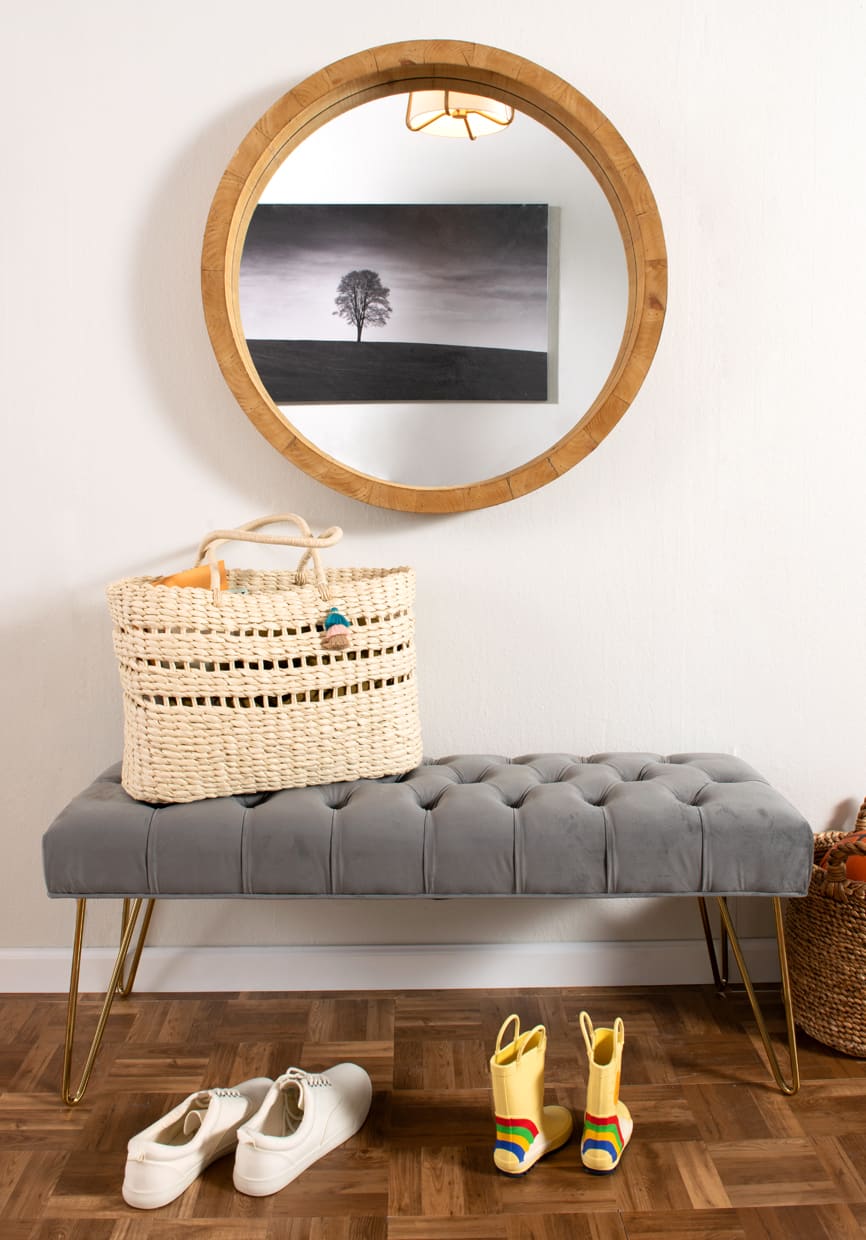 Entryway with round mirror, gray tufted upholstered bench.
