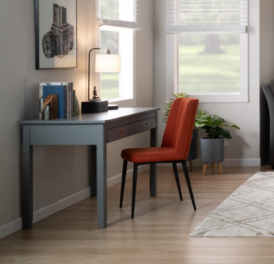 Small blue desk with an orange chair and table lamp and books on the desk.