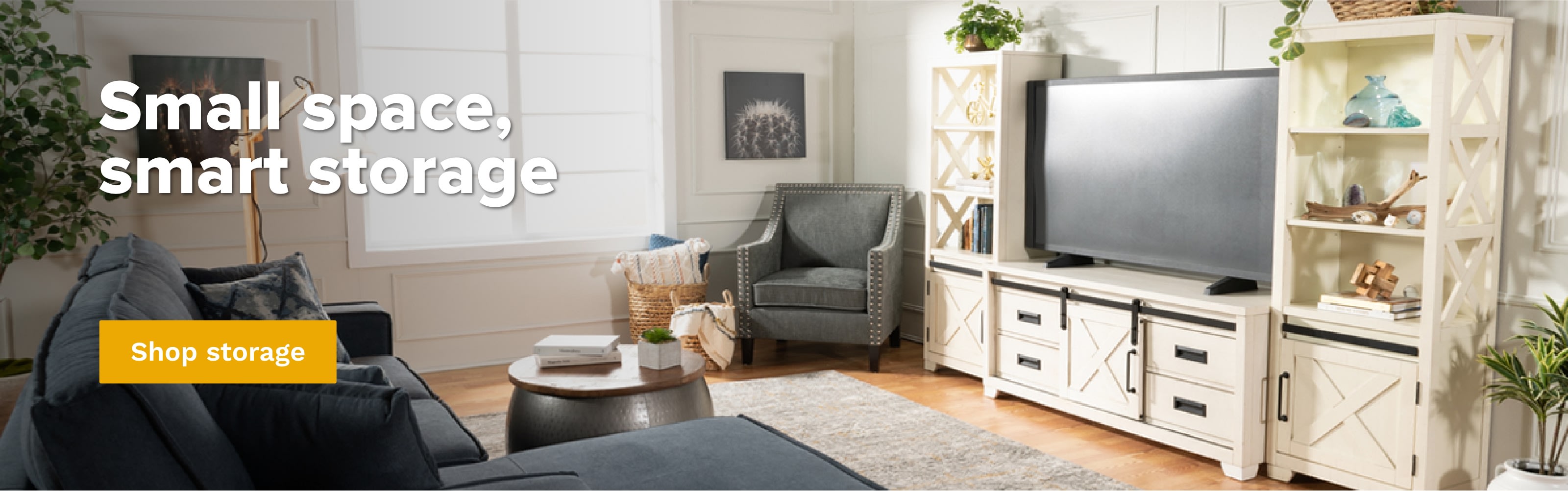 Small space living room with a blue 2 piece left arm facing chaise sectional with a round silver storage ottoman with wooden top, white media center with storage shelves and cabinets.