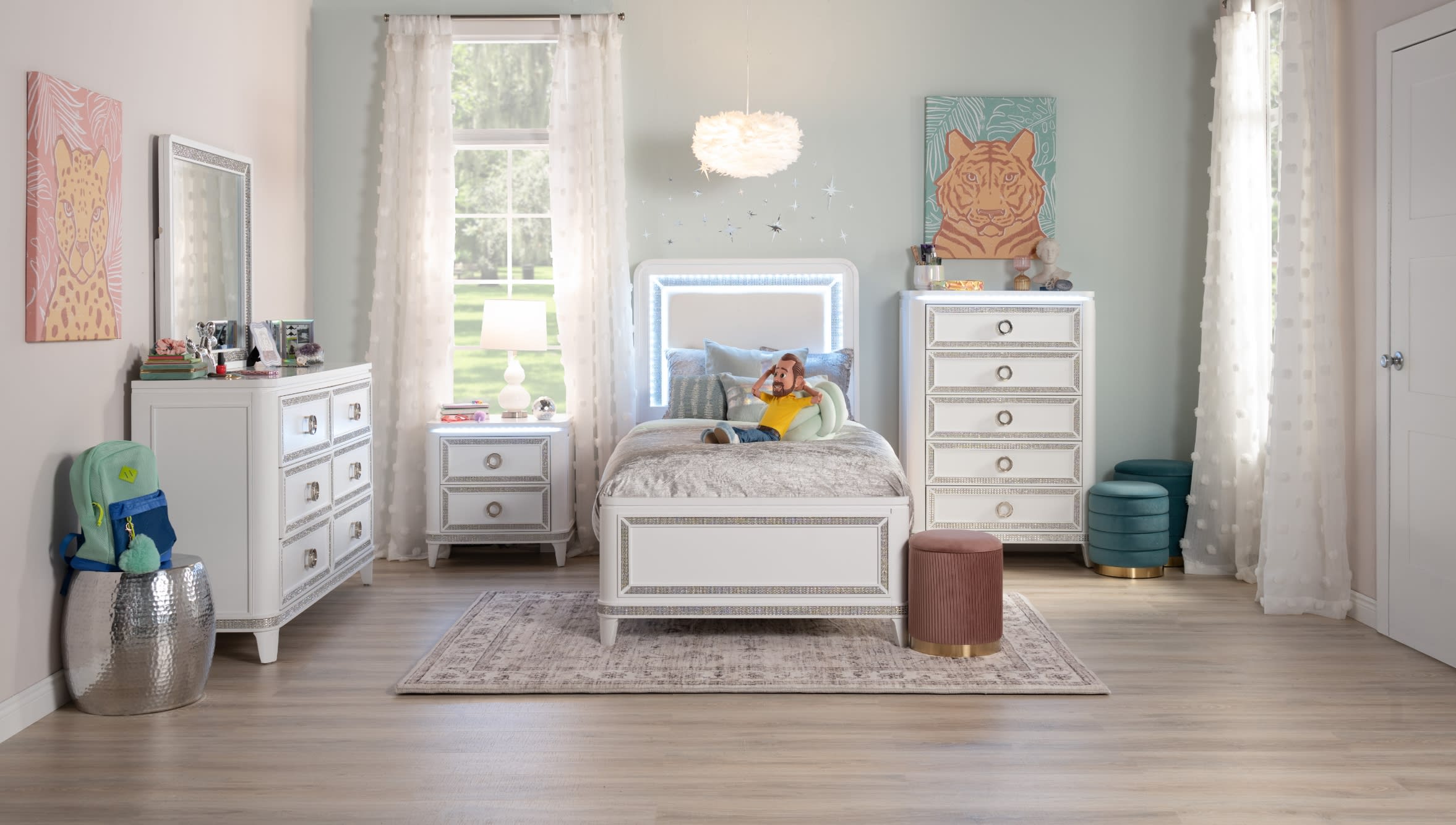 White twin sized bed with illuminated headboard, 6 drawer dresser with mirror, 5 drawer chest, and 2 drawer nightstand on a gray area rug. A fluffy pendant light, abstract tiger artwork, and blush upholstered ottoman decorate the space.