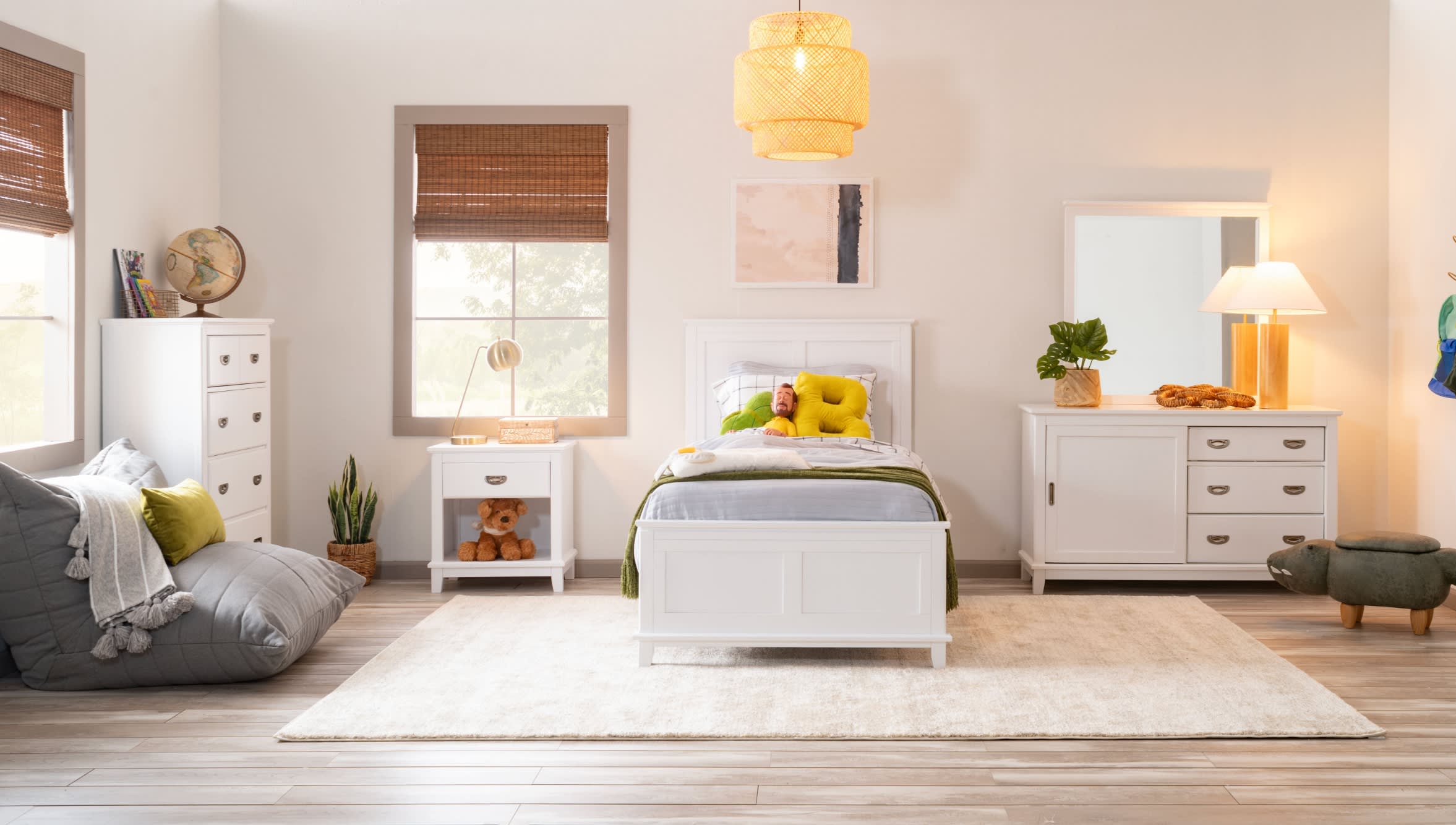 Kids bedroom with white twin sized bed, 3 drawer dresser with mirror and cabinet storage, white nightstand with drawer positioned on a white patterned rug.