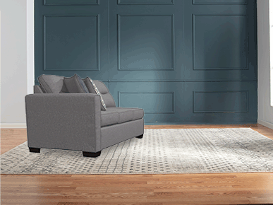 Modern living room with a gray fabric sofa featuring clean lines and multiple cushions, set against a teal paneled accent wall and a patterned area rug on hardwood flooring.
