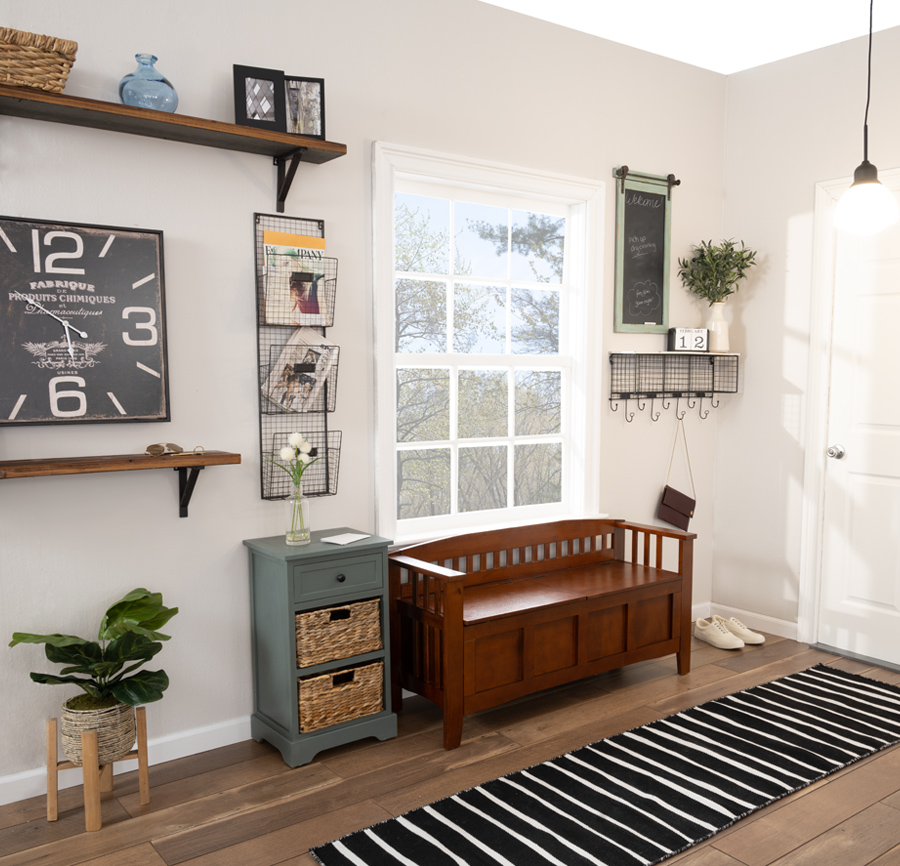 Entryway featuring brown storage bench, 3 drawer accent table, black and white striped runner, 2 wood shelves, coat hooks, and a large square decorative clock.