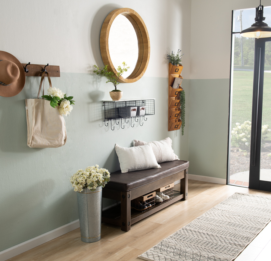 Entryway focused on shelves and coat hooks.  A brown upholstered bench with a shelf for shoe storage, a round mirror, and plush ivory throw pillows complete this coastal inspired design.