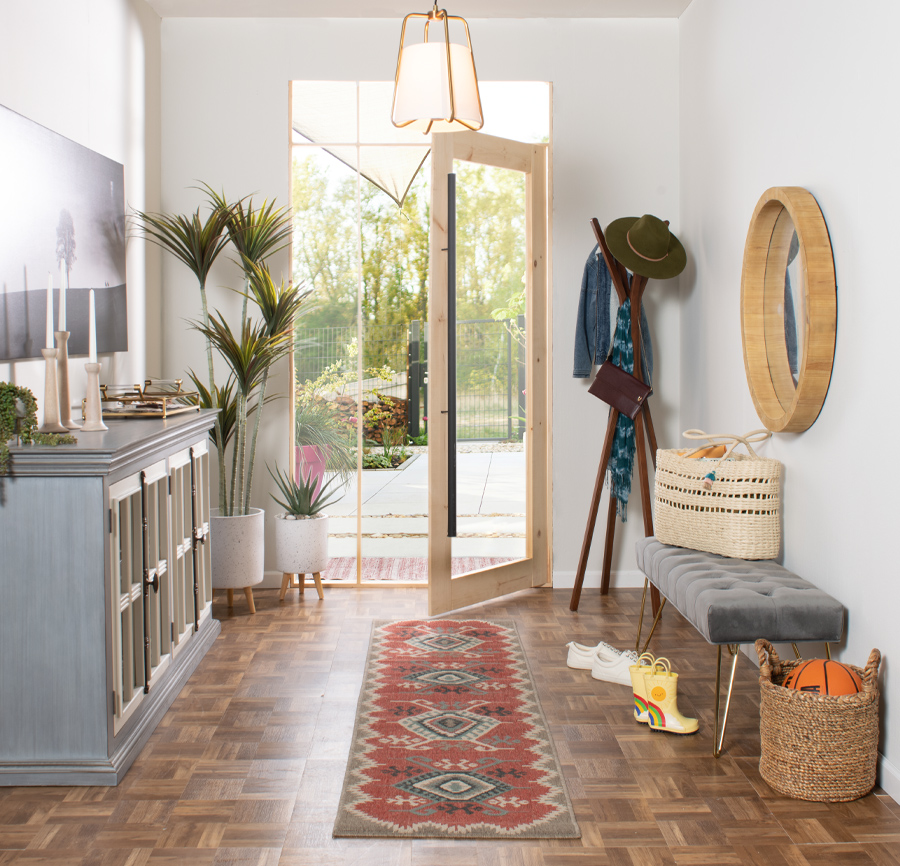 Mudroom focused on Southwestern style runner rug.Coat rack, mirror, and gray cabinet and bench complete the relaxed design.