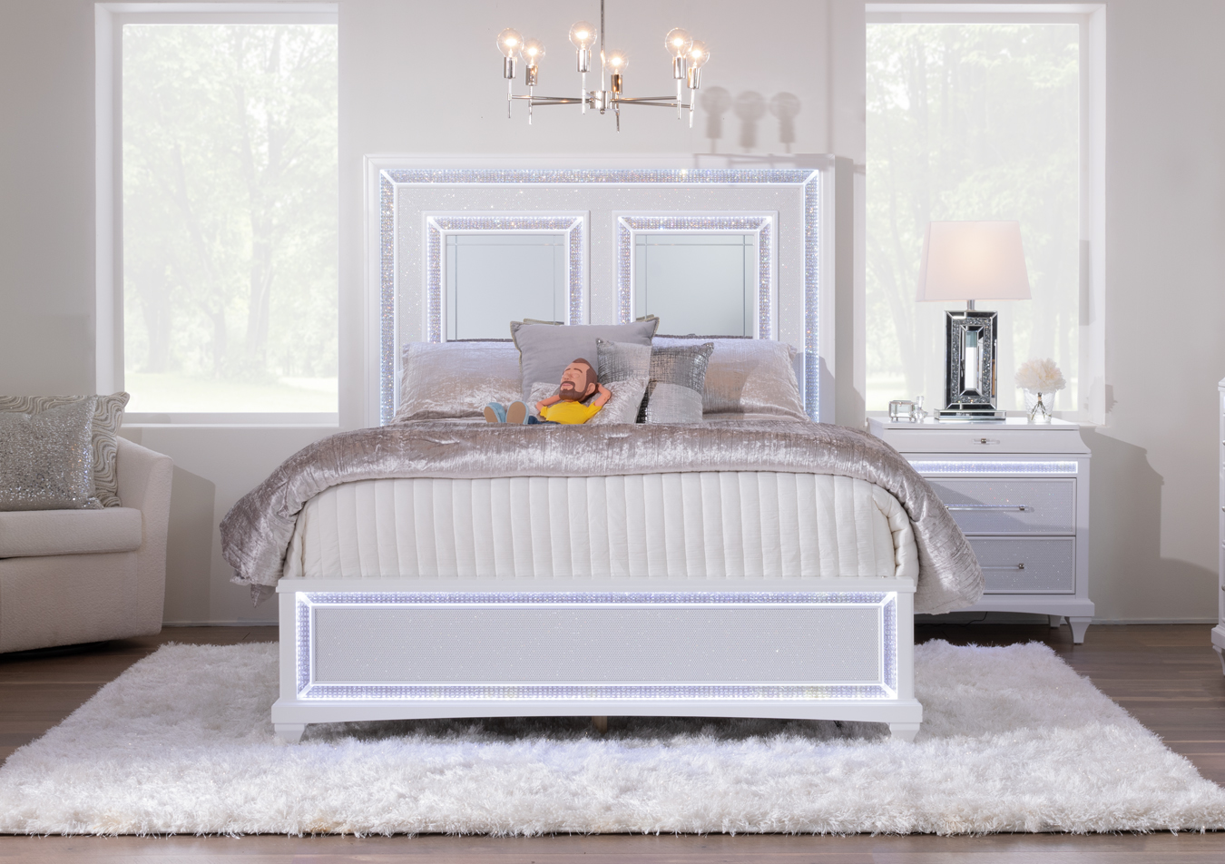 Glamourous pearly white finish with textured trim, LED lighting, and mirror crystals bedroom set with bed and 2 drawer nightstand, atop a white shag carpet with beige upholstered chair, silver accent pillows and silver comforter.