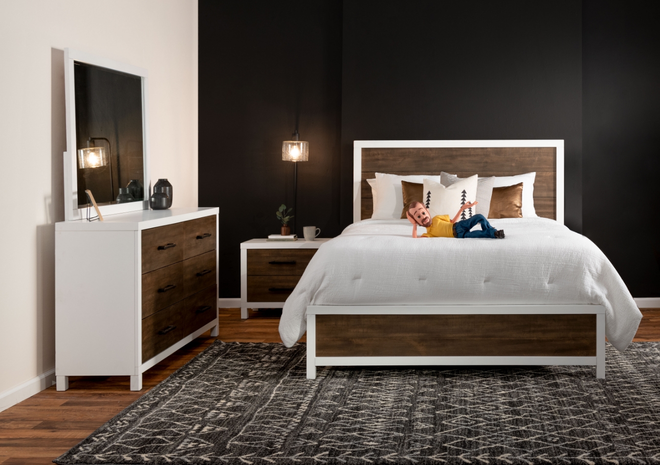 Stylish white and brown two-tone bedroom set with black hardware including a bed, 6 drawer dresser with mirror, and 2 drawer nightstand, anchored on a black and beige floral patterned rug with bronze accent pillows.