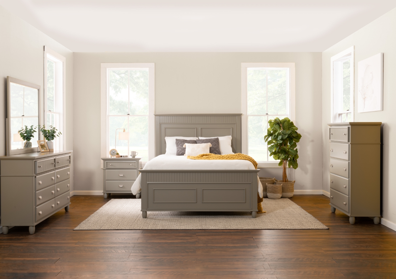 Classic gray bedroom set with bed, 8 drawer dresser with mirror, 5 drawer chest, and 3 drawer nightstand, sitting on a beige carpet with gold throw blanket and gray and white accent pillows.
