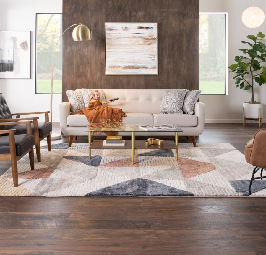 Little Bob with a yellow shirt sitting on a beige faux leather sofa under throw blanket with a remote in his hand.