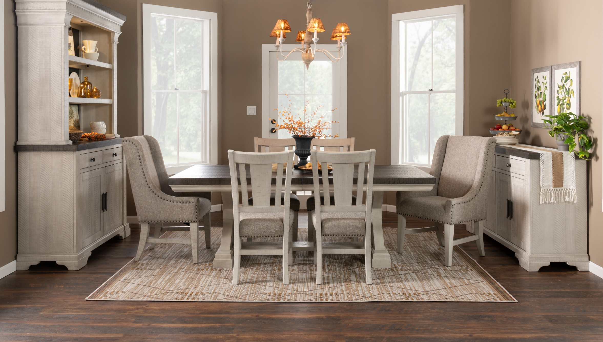 Transitional two tone dining room set with brown tops and white bases, featuring beige upholstered slat back chairs and fully upholstered host chairs, with a china cabinet and server all on top mahogany wood floors and beige area rug.
