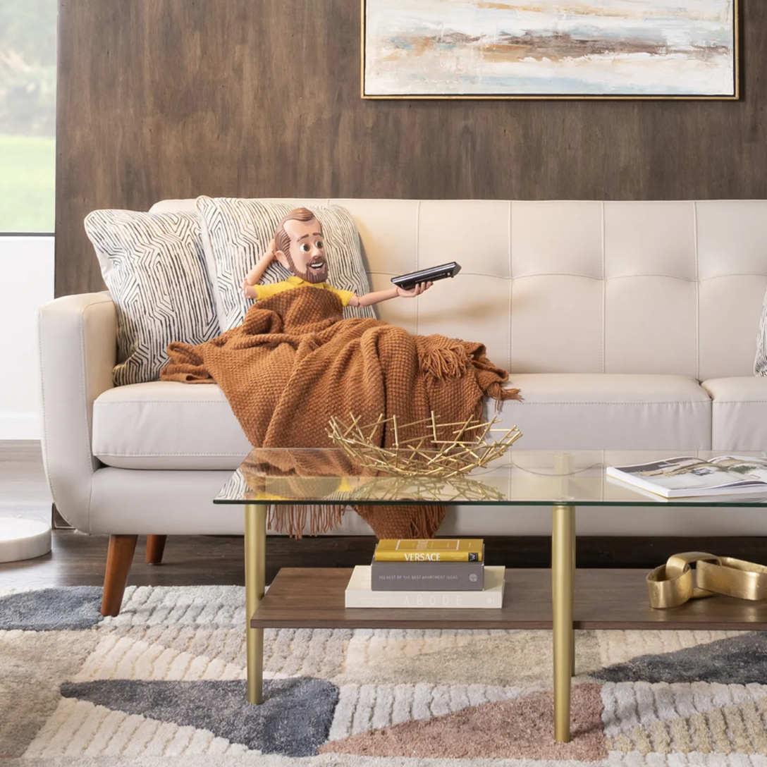 Little Bob with a yellow shirt sitting on a beige faux leather sofa under throw blanket with a remote in his hand.
