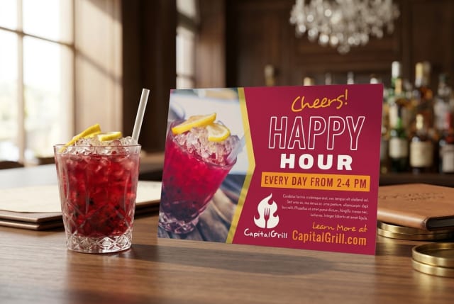 A stack of printed restaurant postcards resting on a wooden bar counter next to a cocktail glass