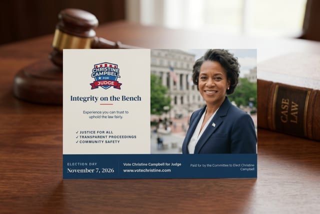 A stack of political campaign postcards for a judge candidate sitting on a wooden desk next to outgoing mail.